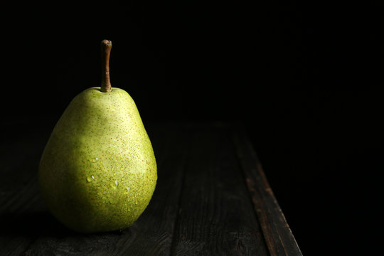 Ripe pear on wooden table against dark background. Space for text