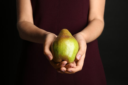 Woman holding ripe pear on black background, closeup
