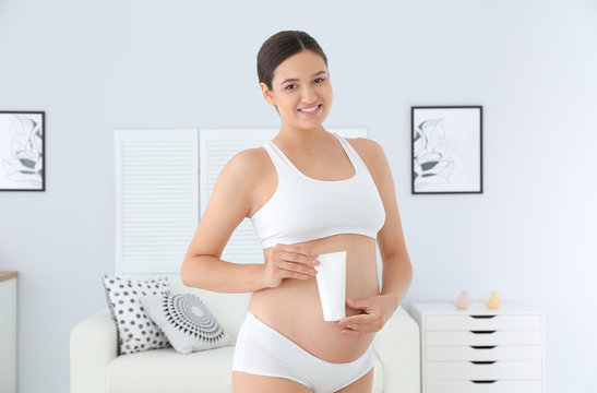 Pregnant woman holding body cream at home