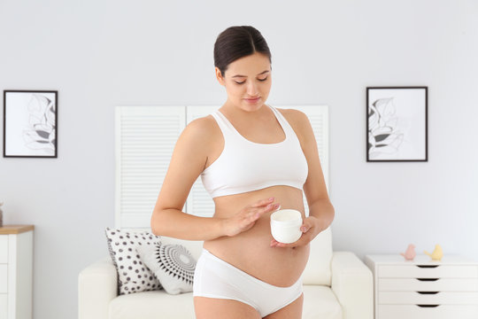 Pregnant woman holding body cream at home