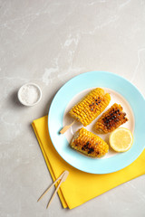 Plate with delicious grilled corn cobs on light table, top view. Space for text