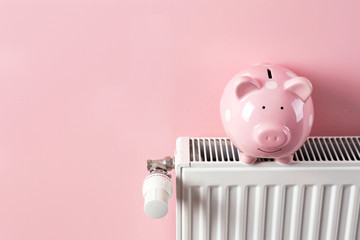 Heating radiator with piggy bank on color background. Space for text