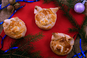Cookies for Christmas 2019 in the form of puff pastry pigs, laid on a red napkin next to Christmas decorations.