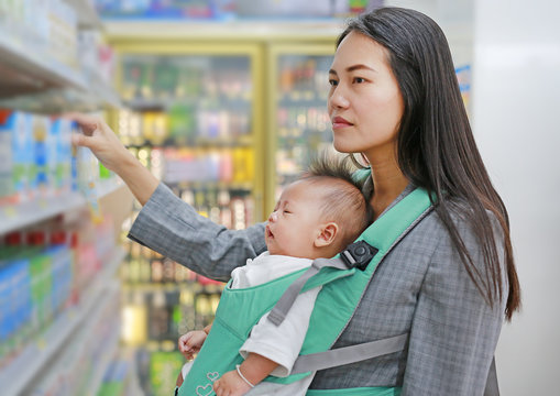 Young business woman in Convenience Store while carrying her baby boy by ergonomic baby carrier.