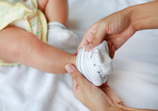 Mother hands trying to put a socks for her infant baby on the bed.