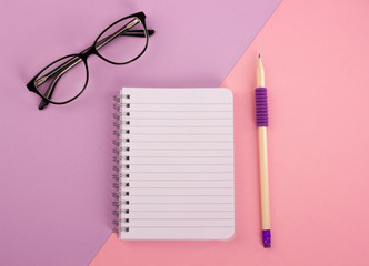Spiral notepad, pencil and glasses on pastel background.