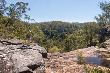 Female, baby boomer, hiker taking in the view from the top of the virtually dry waterfall at the top of Rainbow Waters (Gudda Gumoo) gorge in Blackdown Tableland National Park, Queensland, Australia.