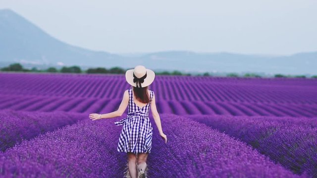 Happy Young Woman Running in Lavender Field at Dusk. SLOW MOTION 120 FPS. Joyful girl in a straw hat enjoying life in endless blooming lavender fields. Plateau du Valensole, Provence, France. 