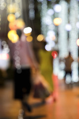 Blurry background image of defocused outdoor Christmas decorations with colorful lights and people in busy city street at night