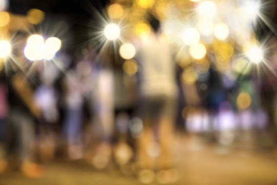 Blurry background image of defocused outdoor Christmas decorations with colorful lights and people in busy city street at night