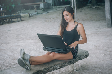 Happy woman with laptop enjoying in swing on tropical beach