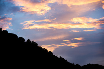 colorful cloudy sky with blue orange and silhouette tree canopy on mountain at bottom