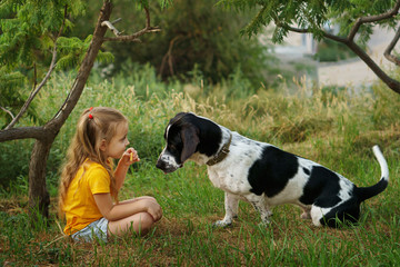 Little girl and mongrel dog outdoors. Child and pets are sitting on lawn. Children and animals.