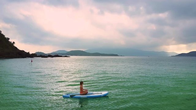 girl drifts on paddleboard in pose Half Lotus among ocean