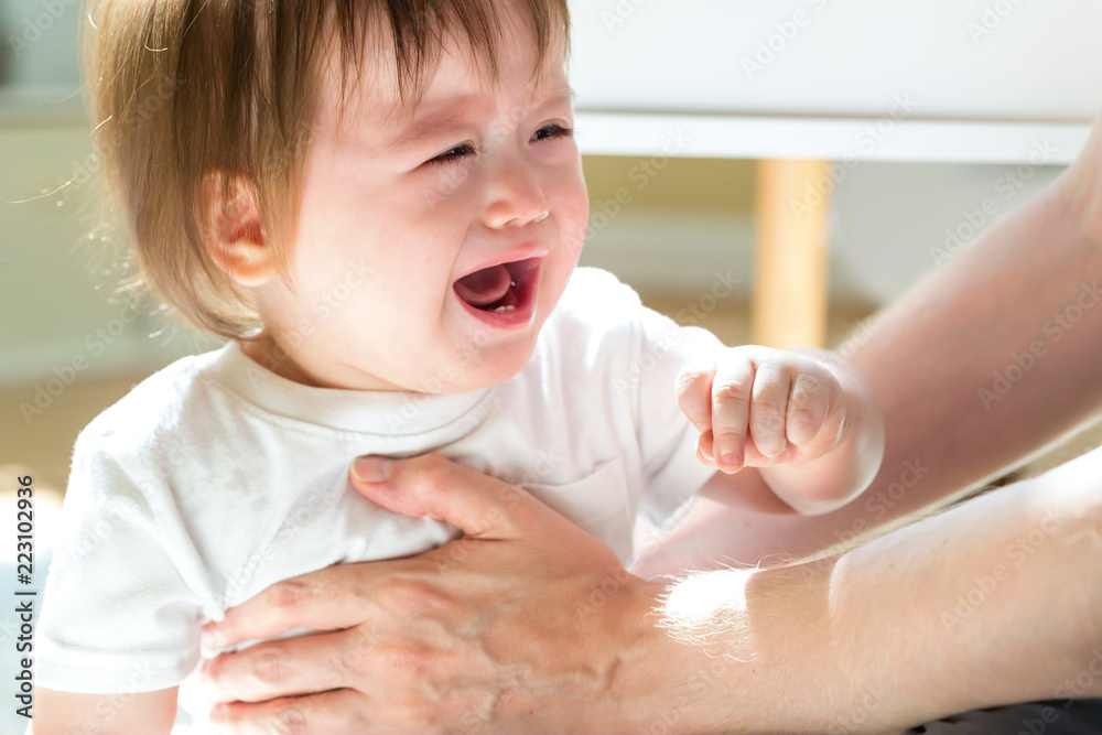 Sticker upset toddler boy crying while being held by his father