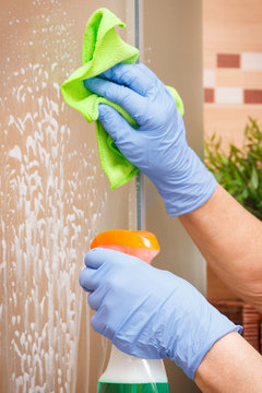 Hand Of Senior Woman Cleaning Glass Shower In Bathroom Using Microfiber Cloth And Detergent