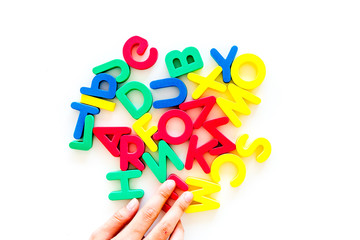 Children learn read concept. Hand hold plastic letters of toy alphabet on white background top view