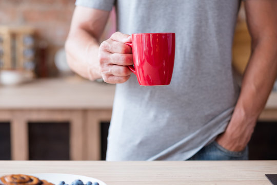 traditional morning hot beverage. quick and easy breakfast. man holding tea or instant coffee drink in a red mug standing in the kitchen.