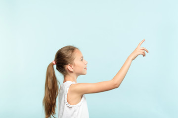 thoughtful girl reaching and wanting to press invisible button on the right. interface or virtual screen concept. free space for advertisement or text. portrait child on blue background.