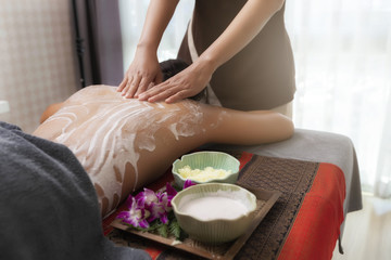 Obraz na płótnie Canvas Spa therapist applying scrub salt and cream on young woman back at salon spa. Hands massaging female back with scrub.