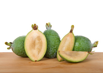 Whole Pineapple guava on a wood table with sliced fruit in half and quarters.