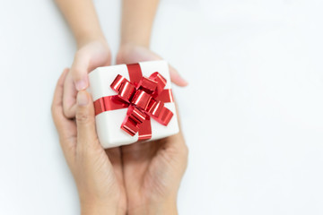 Daughter gives a gift to mother.  White box with red bow in the girl hands and mother hands for give a gift