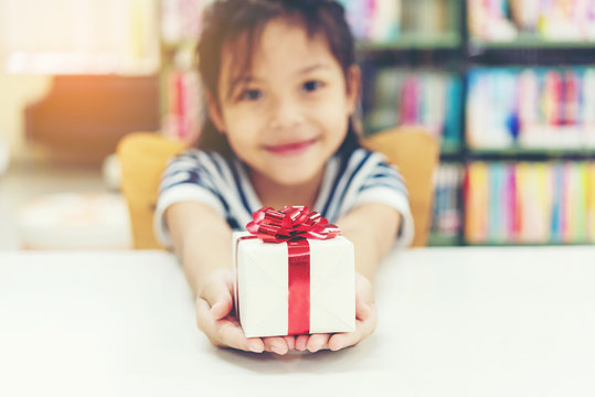 Gift box for kids girl.   White box with red bow in the girl hands for give a gift in the library