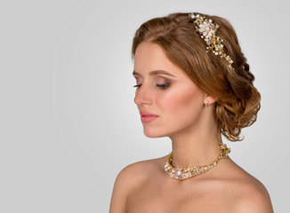 Close up portrait of the young woman bridg in a necklace from pearls and in a crown on gray background in studio