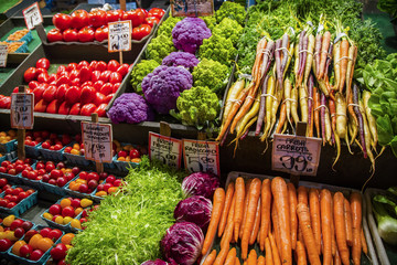 A variety of fruits and vegetables for sale at a grocery store. Fresh organic carrots, cabbage, frisee lettuce, tomatoes, and cauliflower all deliciously displayed