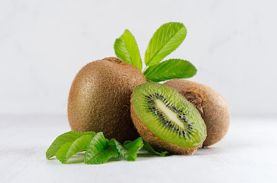 Ripe fleshy green kiwi with juicy slice, young leaves on soft light white table, closeup. Tropical fruits background.