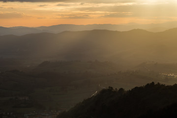 Sunrays coming over a valley in Umbria (Italy) with some plants in the foreground