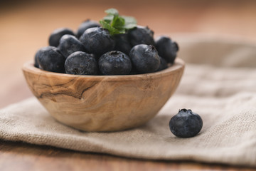 Fresh blueberries in wood bowl on table with napkin slightly toned