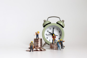 Miniature worker people with alarm clocks and piles of coins.