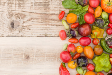 Closeup of multi-colored fresh organic vegetables: paprika, tomatoes, and herbs on natural wooden background. Healthy food concept