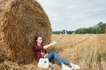 Naklejka na ściany i meble young girl makes selfie on smartphone on the background of haystack