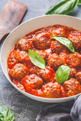 Tasty beef meatballs in tomato sauce with spices and fresh basil on a kitchen table. Food photography, vertical shot, European cuisine.