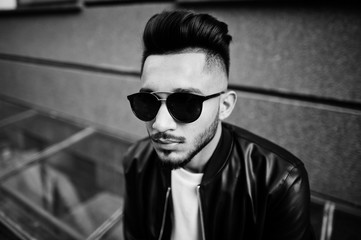 Stylish indian beard man at black leather jacket and sunglasses. India model posed outdoor at streets of city.