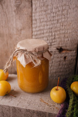 Homemade apple jam in bank in the autumn background with ripe apples and green leaves on the old wooden table, vertical photo
