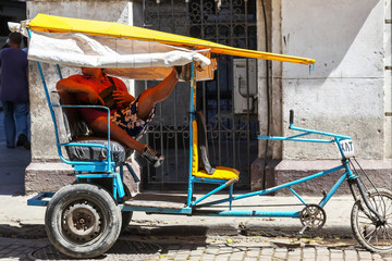 Fototapeta na wymiar Havana / Cuba - August 15, 2015: Vintage coach strange bicycle with driver resting leg up on it, outdoors, sunny day.