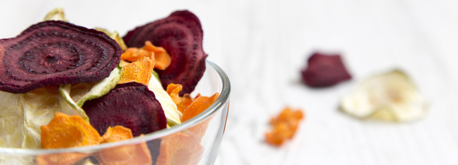 Full bowl of veggie chips on white wooden surface, side view. Close-up.