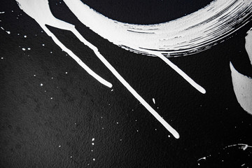 Texture of white paint on a black wall, graffiti, street art. Traces of paintbrush and brush