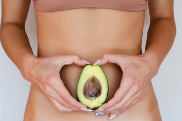  a woman holds an avocado near the stomach in the shape of a heart