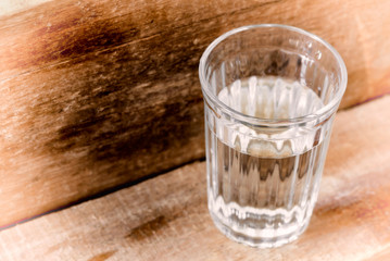 One glass of water, illuminated with natural light, on a wooden plank