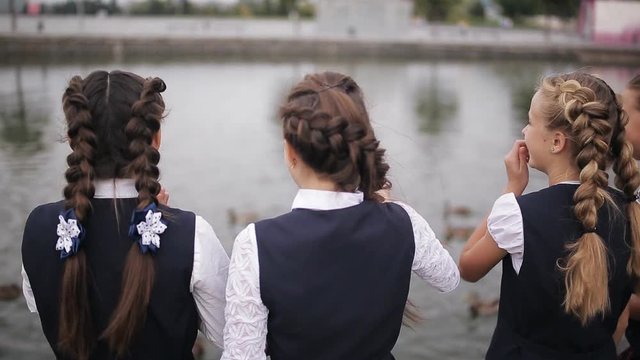 Students in school uniform feeding ducks in a pond in the school yard. Girls College coeds wearing the same school uniform feed the ducks in the pond on campus