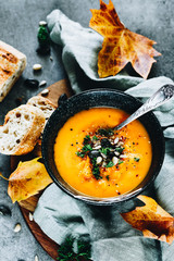 Vegan Creamy Delicious Pumkin Soup with fresh vegaetables and sliced of bread and fall leaves over a dark background.