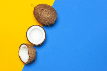 Ripe coconut on yellow and blue colored background, minimal flat lay style top view with copy space. Pop art design, creative summer and food concept. Tropical fruit whole and half abstract background