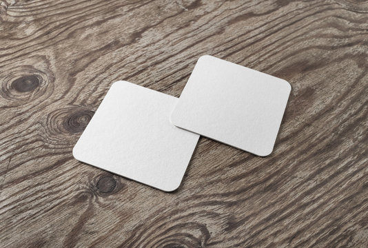 Photo of two blank white beer coasters on wood table background. Blank template for your design.