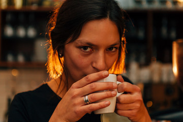 frontal portrait of a young beautiful woman drinking from a cup of coffee and looking at the camera