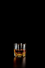 Single glass of whisky or whiskey with ice on black background.