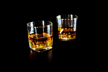 Two glasses of whiskey or whisky with ice on black background.